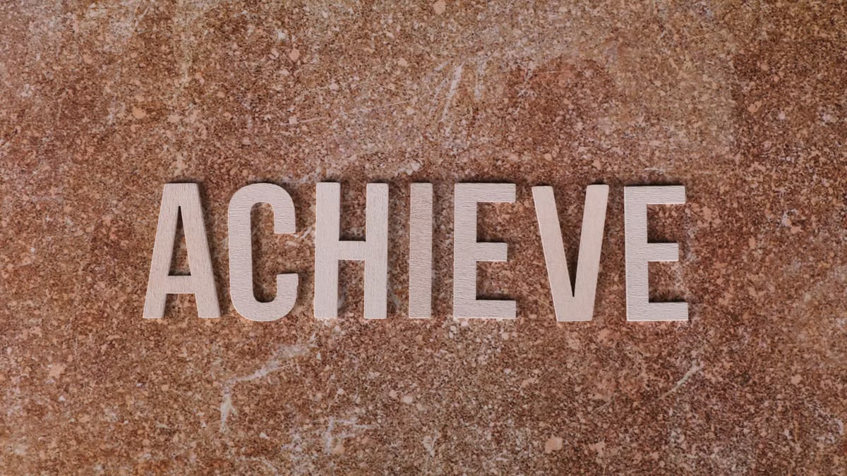 Wooden letters spelling 'ACHIEVE' on a textured brown surface, conveying motivation and success.
